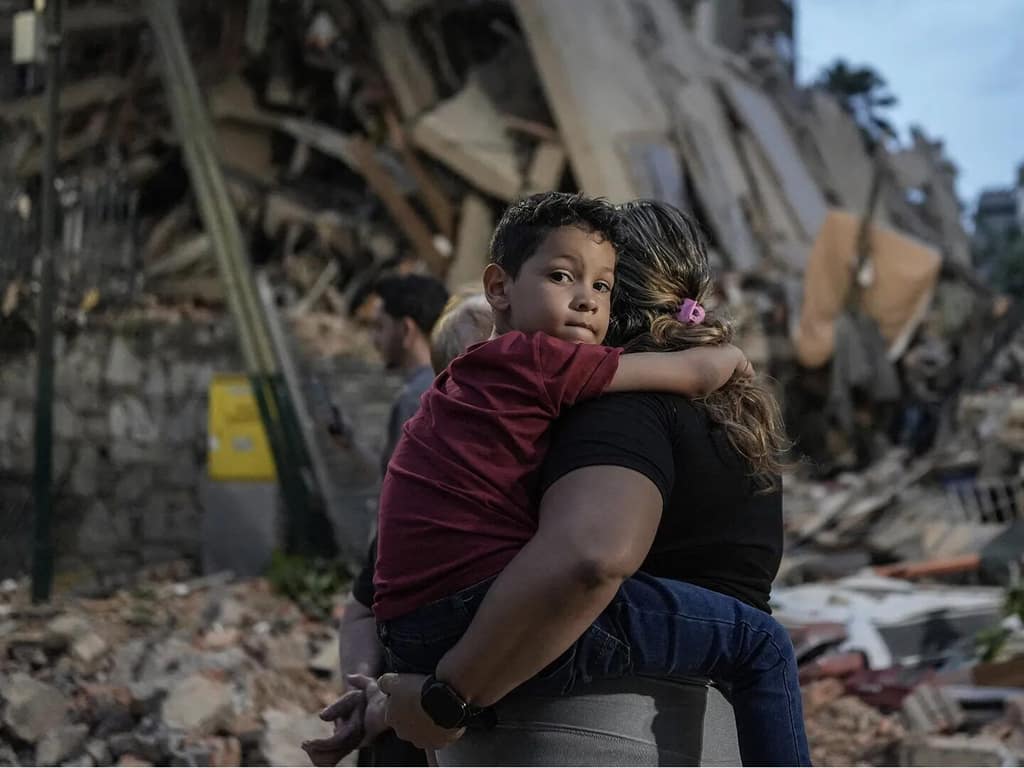 A mother holding her child in front of a collapsed building in Venezuela